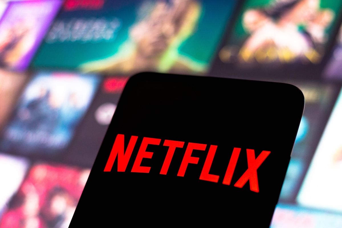 a smartphone is pictured with the netflix logo in the foreground, with a mosaic of artwork from Netflix shows in the background 