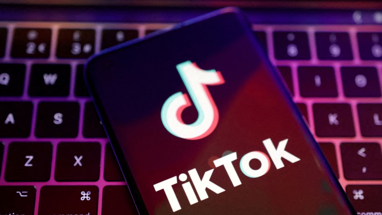 a smartphone with the tiktok logo on-screen is pictured on a computer keyboard