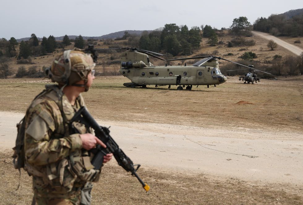 A soldier, a Boeing CH-47 Chinook military transport helicopter and a Boeing AH-64 Apache attack helicopter of the U.S. Army 12th Combat Aviation Brigade participate in the Allied Spirit 25 military exercise