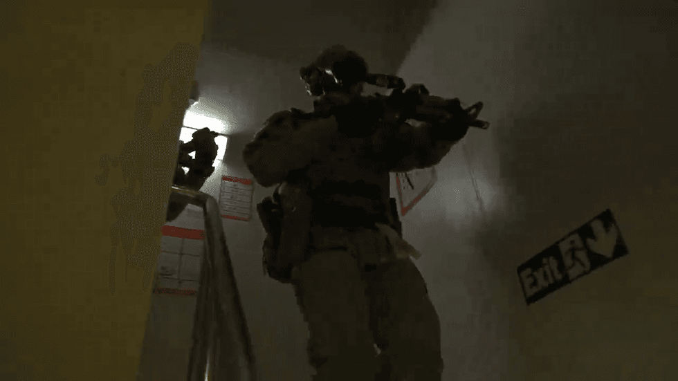 A squadron of troops descend down a stairwell while a cameraman is ahead of them
