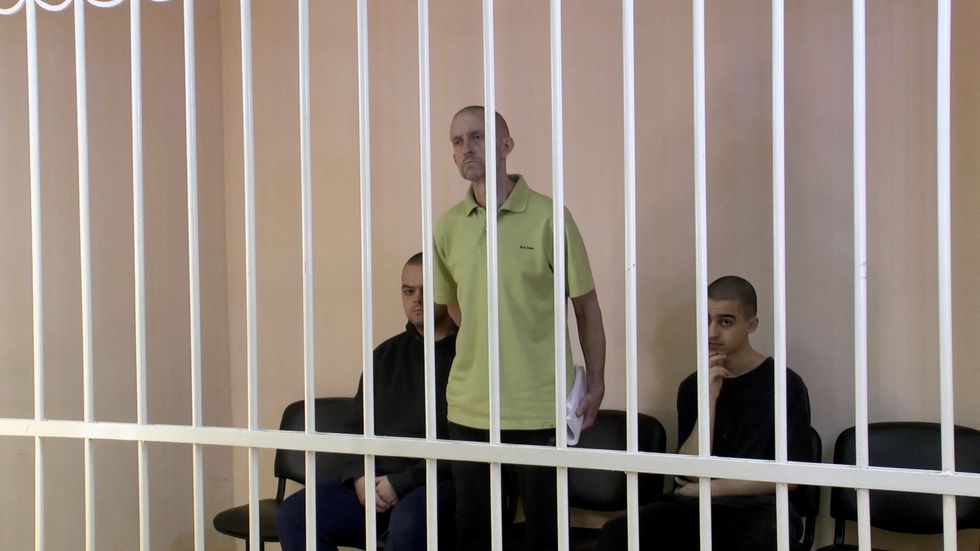 A still image, taken from footage of the Supreme Court of the self-proclaimed Donetsk People's Republic, shows Britons Aiden Aslin, Shaun Pinner and Moroccan Brahim Saadoun captured by Russian forces during a military conflict in Ukraine, in a courtroom cage at a location given as Donetsk, Ukraine.