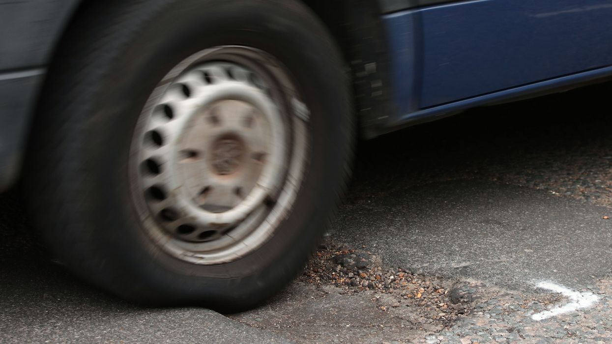 A stock image of a car driving over a pothole