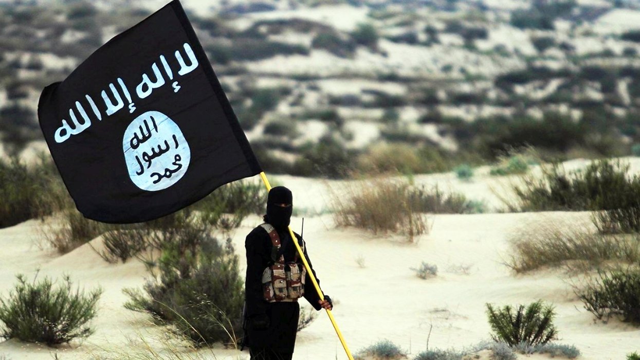 A stock image of a masked Islamic State soldier poses holding the ISIL banner somewhere in the deserts of Iraq or Syria