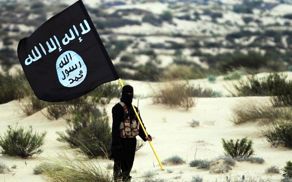 A stock image of a masked Islamic State soldier poses holding the ISIL banner somewhere in the deserts of Iraq or Syria
