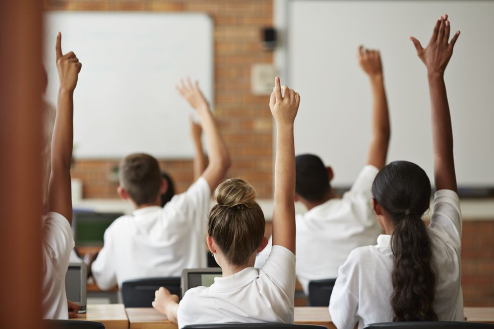 A stock image of children raising hands in class