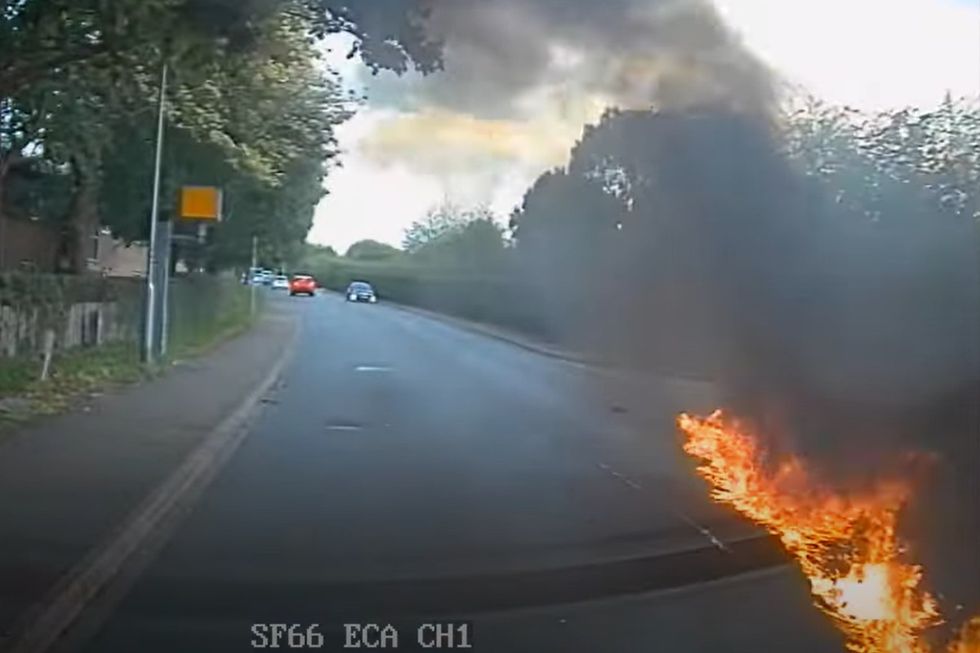 A streak of flaming oil can be seen on the road after the crash