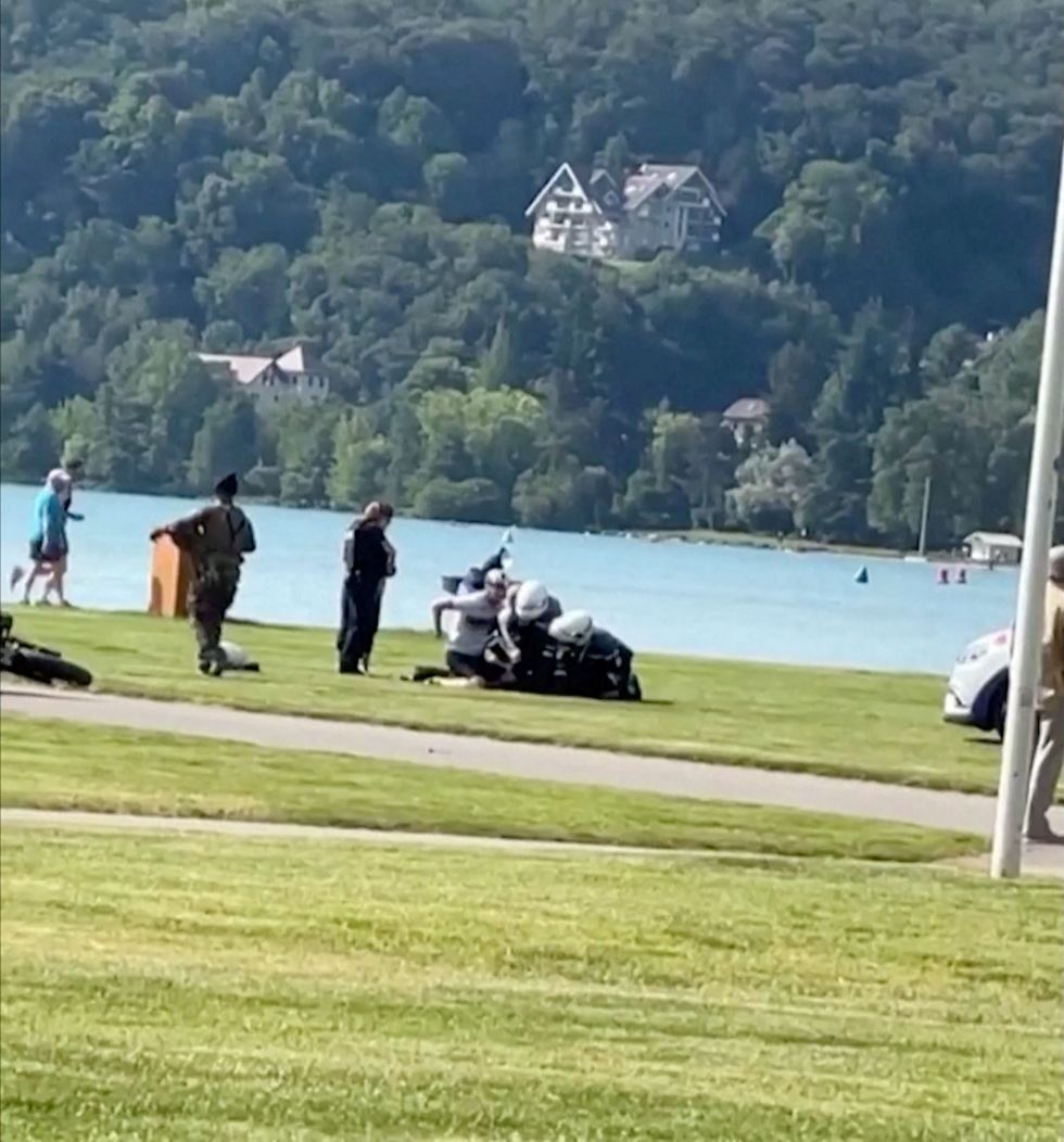 A view shows police appearing to arrest someone at the site where a person wounded four children and an adult in a knife attack in a park in Annecy