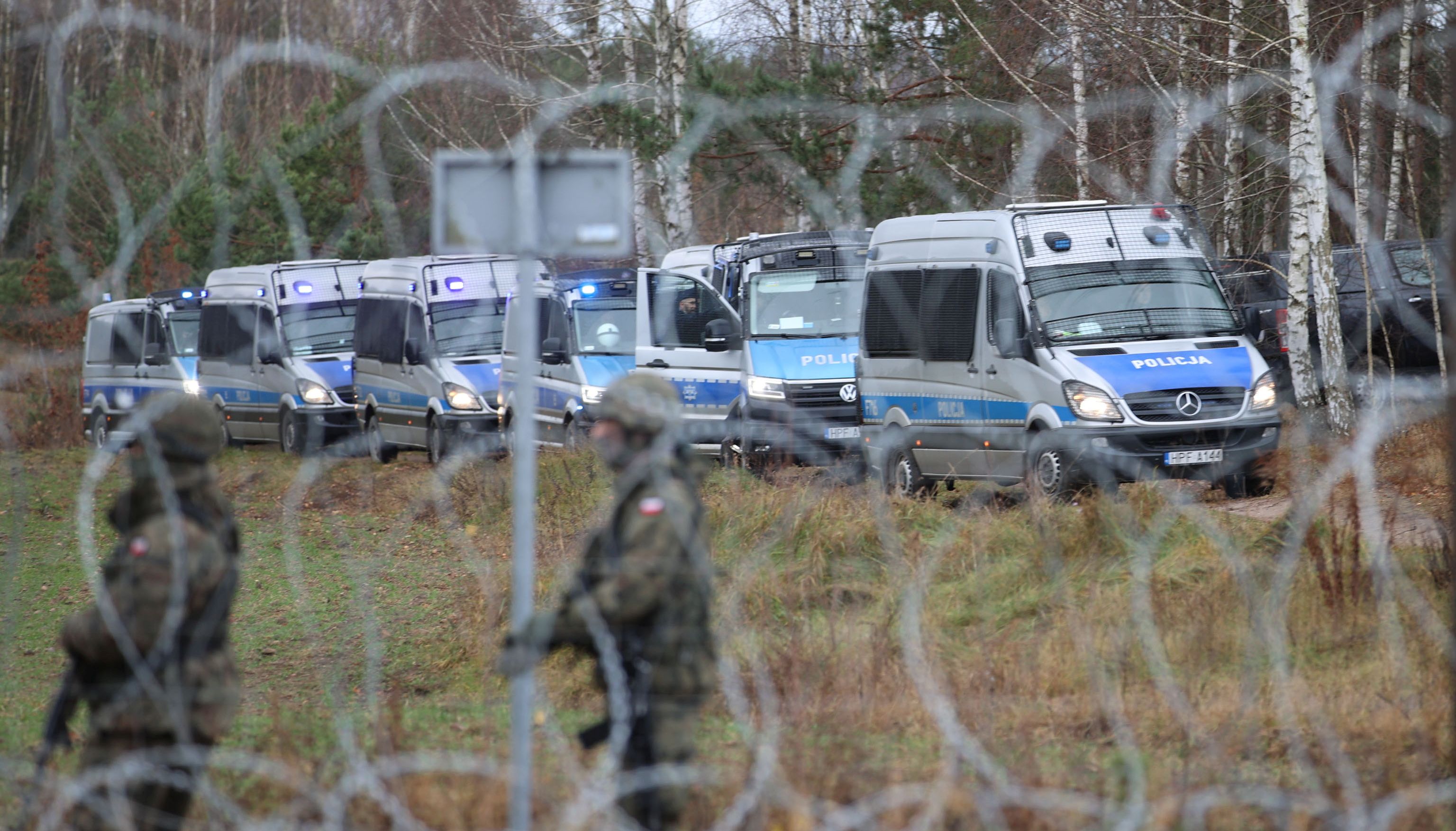 A view through a barbed wire fence shows Polish police minivans as hundreds of migrants gather on the Belarusian-Polish border in an attempt to cross it in the Grodno region, Belarus November 8, 2021.