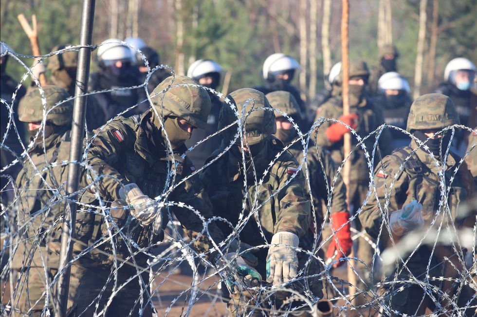 A view through a barbed wire fence shows Polish service members as hundreds of migrants gather on the Belarusian-Polish border in an attempt to cross it in the Grodno region, Belarus November 9, 2021.