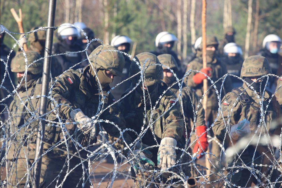 A view through a barbed wire fence shows Polish service members as hundreds of migrants gather on the Belarusian-Polish border in an attempt to cross it in the Grodno region, Belarus November 9, 2021.