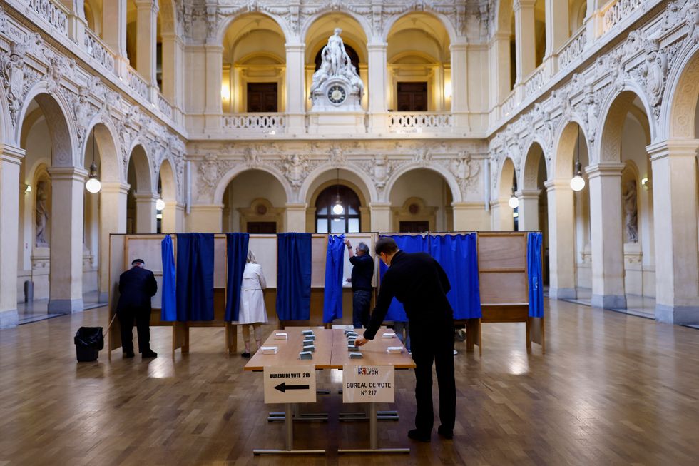 A voter takes a ballot from stacks displayed on tables in the second round of the 2022 French presidential election at a polling station in Lyon, France, April 24, 2022. REUTERS/Stephane Mahe