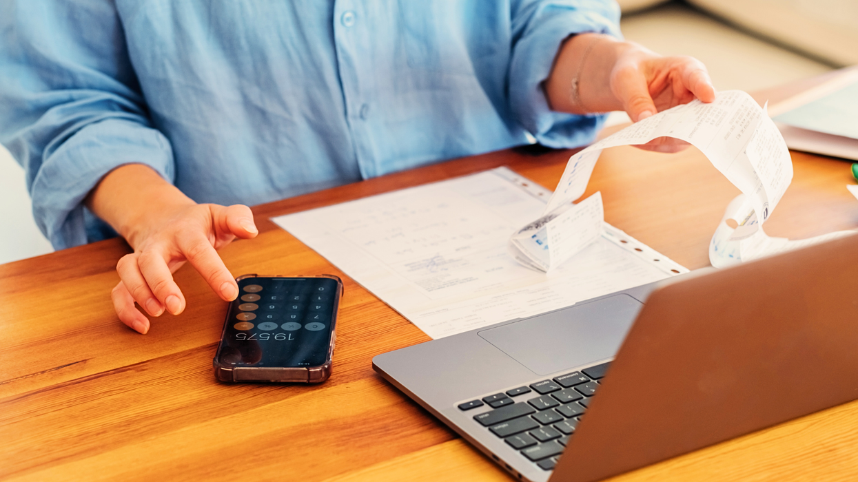 a woman checks receipts for broadband bills and uses a calculator to work out the total price while working on her laptop