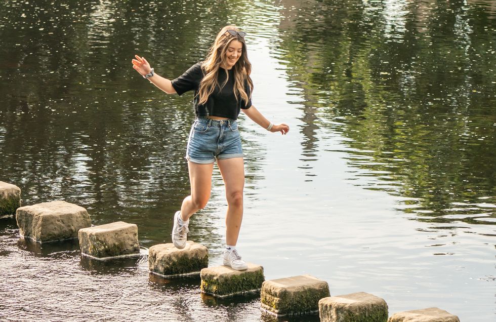 A woman enjoys the sunshine as she walks across stepping stones near Bolton Abbey in Yorkshire
