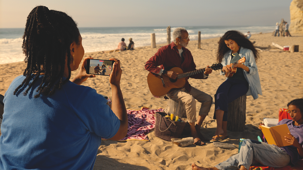 a woman filming with an iphone on the beach captures a band playing together on the beach