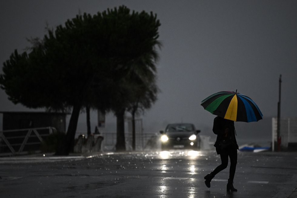 A woman holding an umbrella crosses a street under the rain ahead of storm Ciaran on November 1