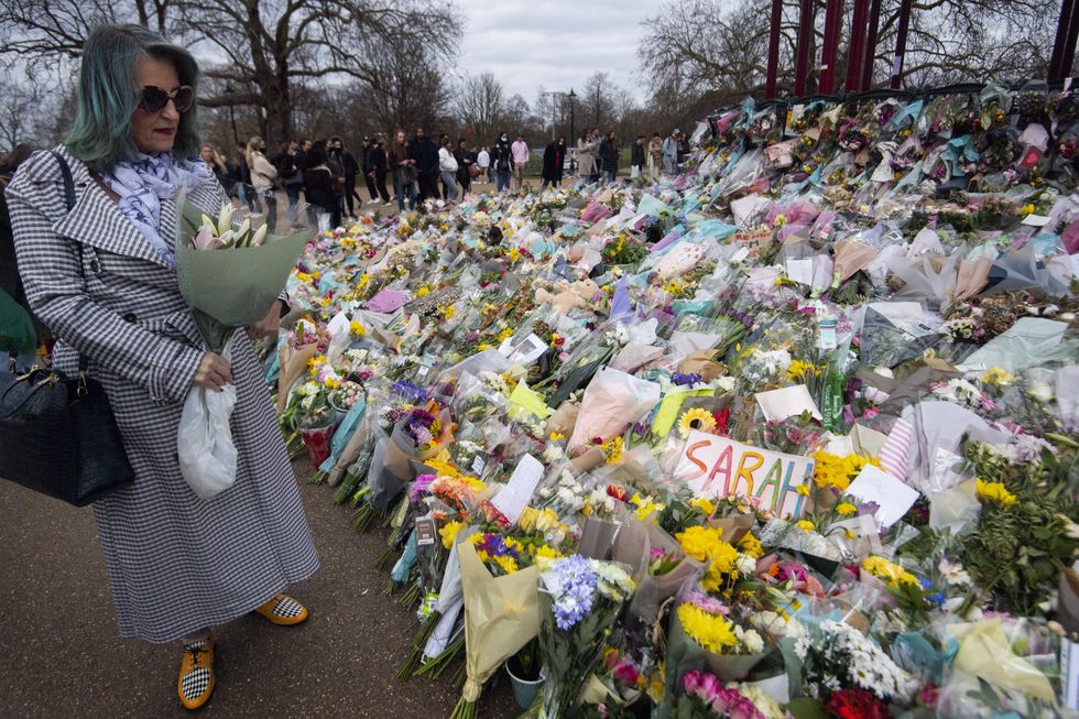 A woman holding flowers looks at floral tributes left at the bandstand in Clapham Common, London, for Sarah Everard. Pc Wayne Couzens, 48, appeared at the Old Bailey in London charged with the kidnap and murder of the 33-year-old. Picture date: Sunday March 21, 2021.