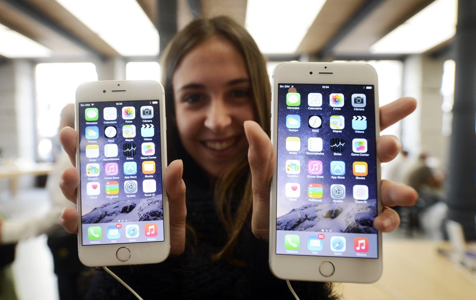 a woman holding the iphone 6 and iphone 6 plus in an apple store on launch day