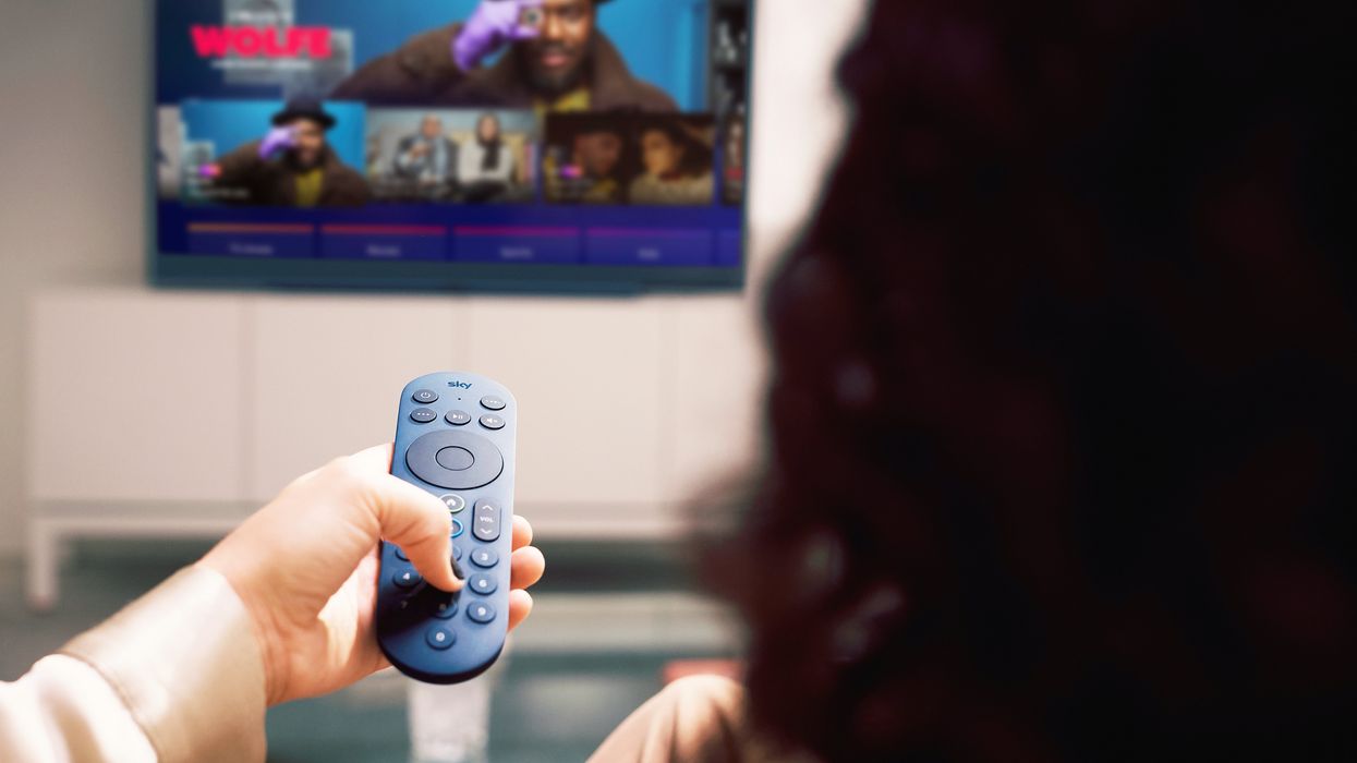 a woman holds a blue remote pointed at a sky glass television