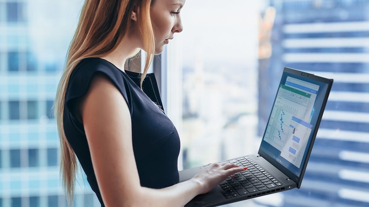 a woman holds a lenovo laptop by the window and types on the keyboard