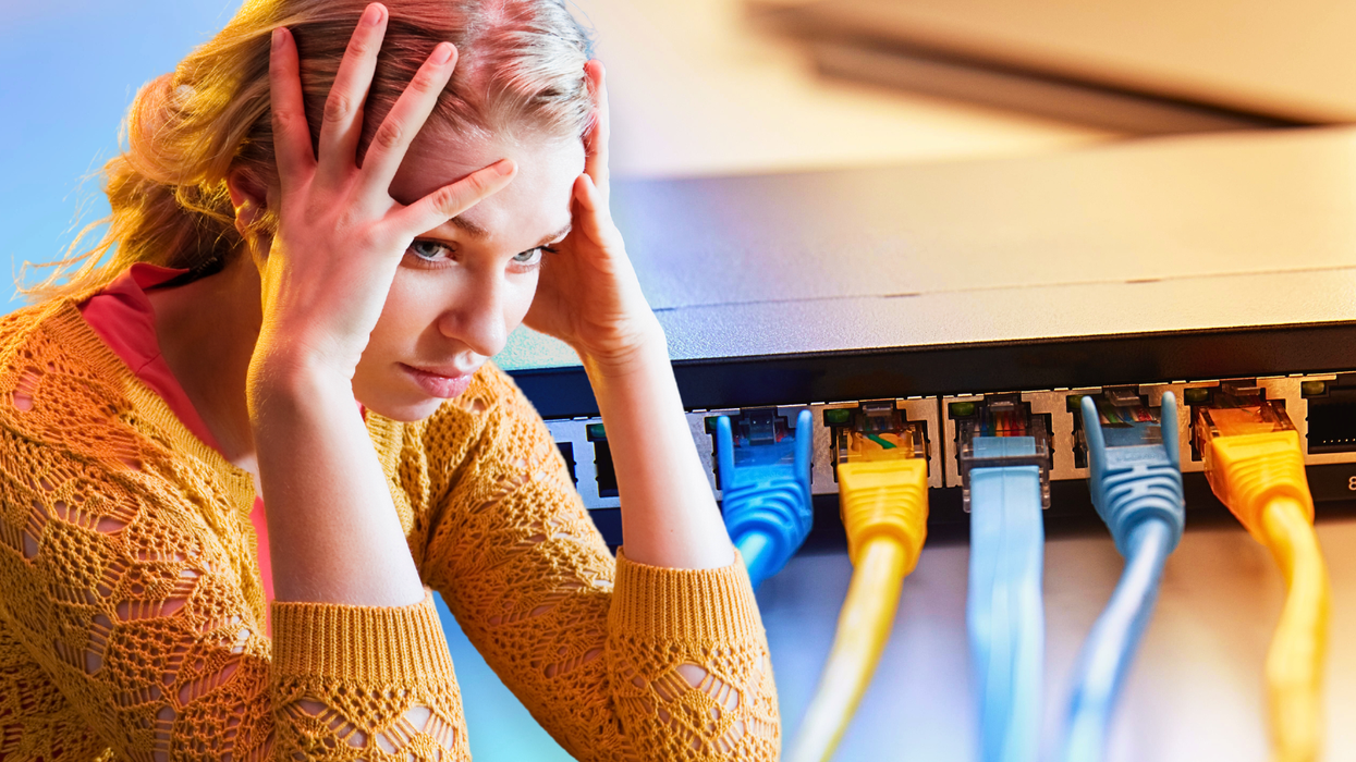 a woman holds head in her hands while a broadband router with ethernet cables connected in pictured in the background
