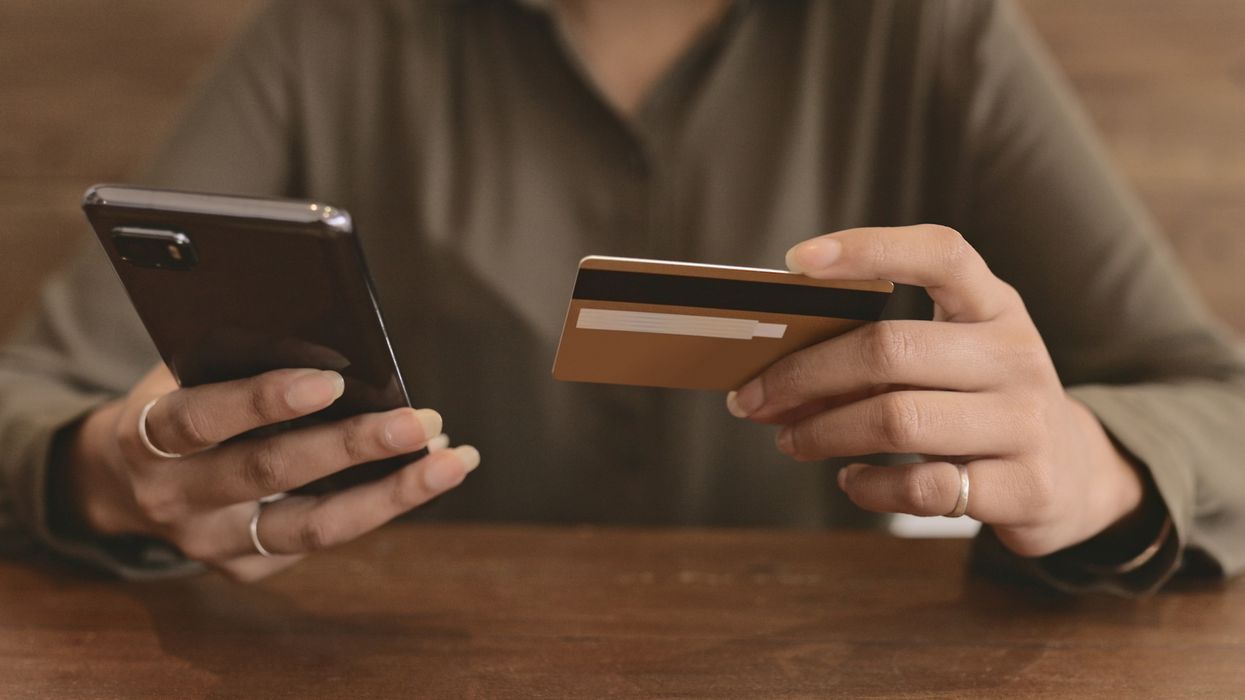 a woman holds her smartphone in one hand and a credit card in the other