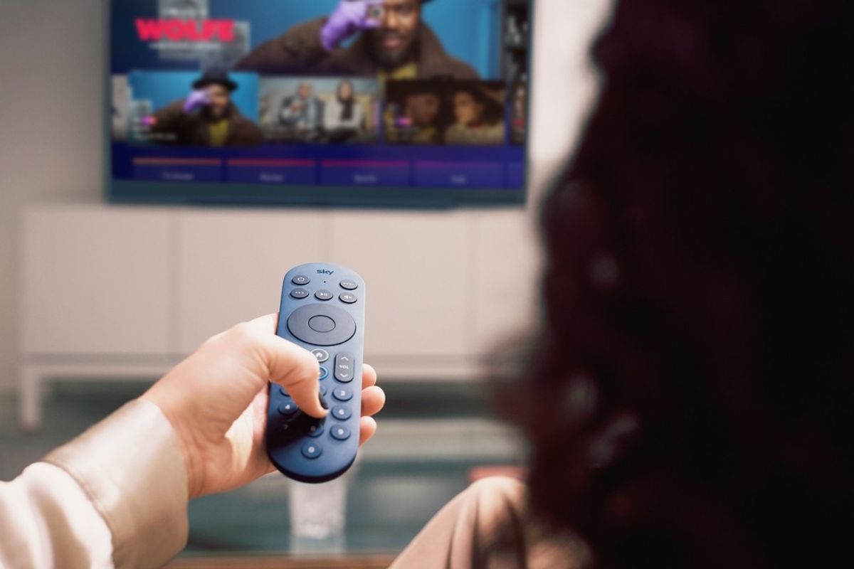 a woman holds out a blue sky glass remote control to change channels   