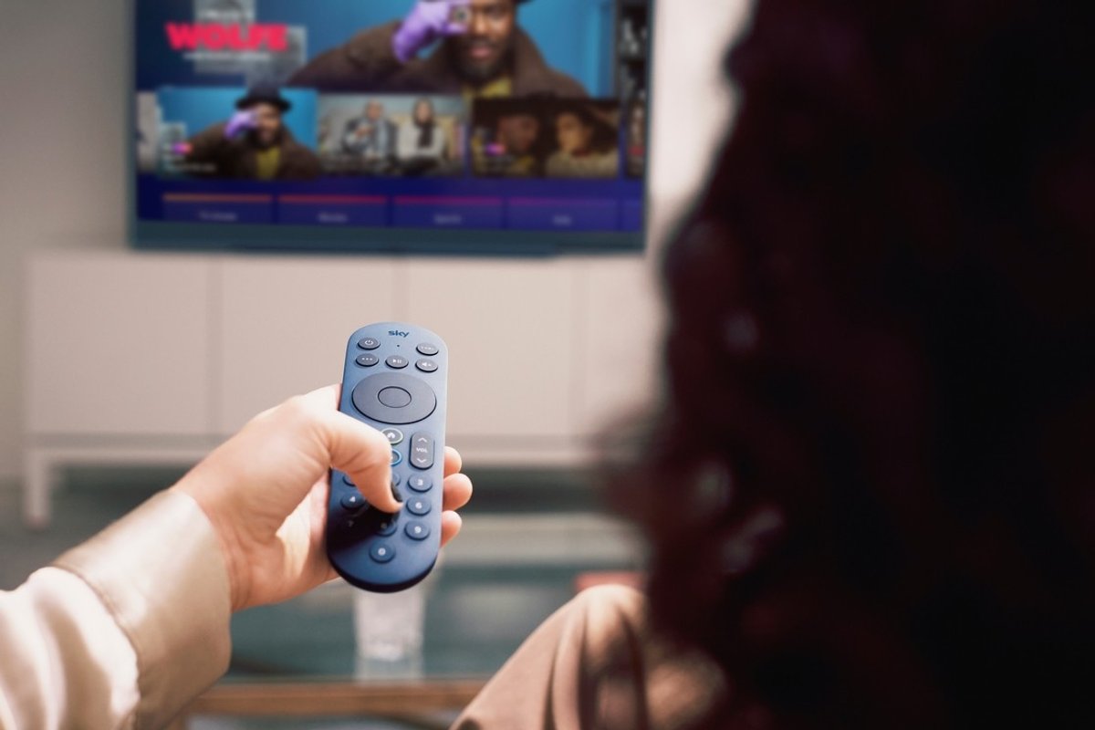 a woman holds out a blue sky glass remote control to change channels