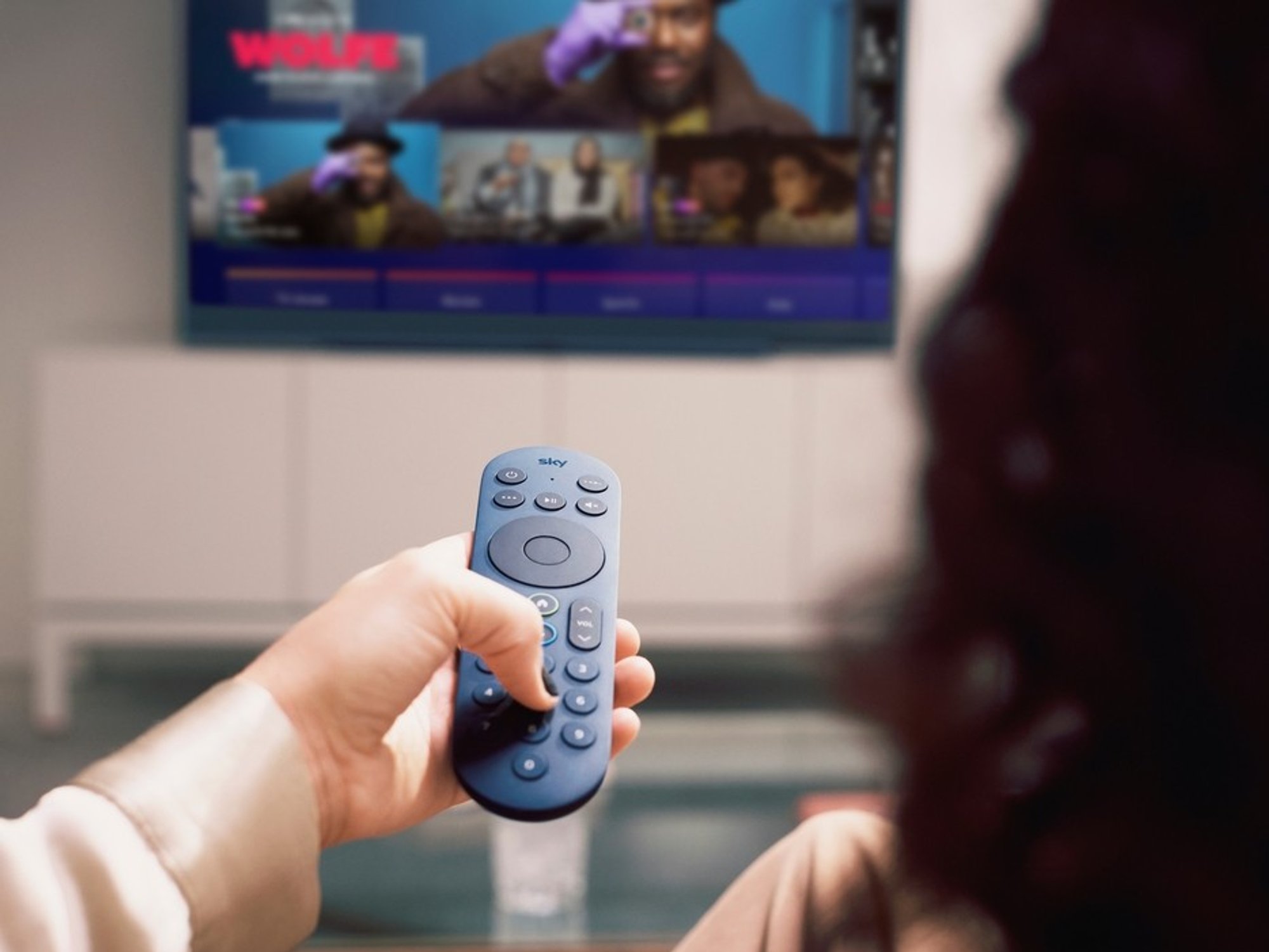 a woman holds out a blue sky glass remote control to change channels