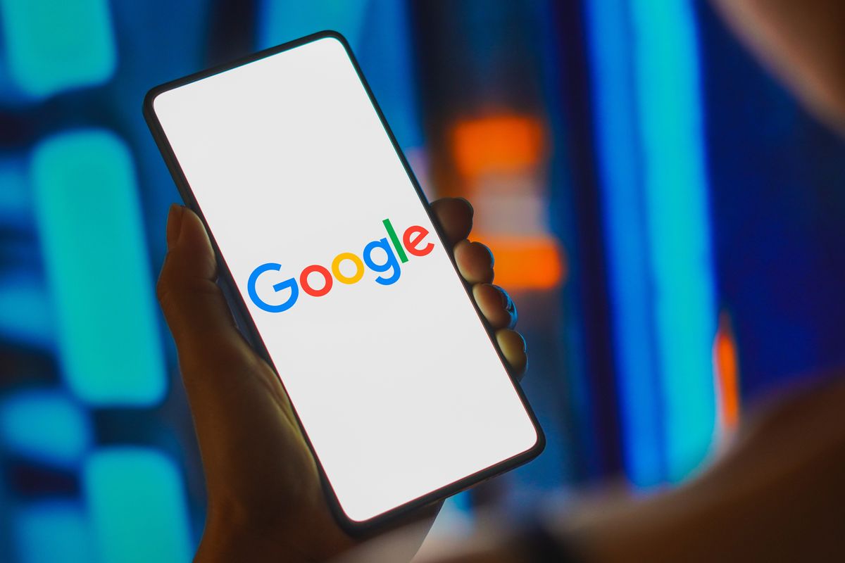 a woman holds out a smartphone with the google logo displayed on screen 