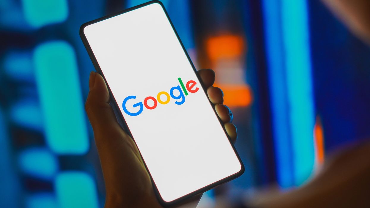 a woman holds out a smartphone with the google logo displayed on screen