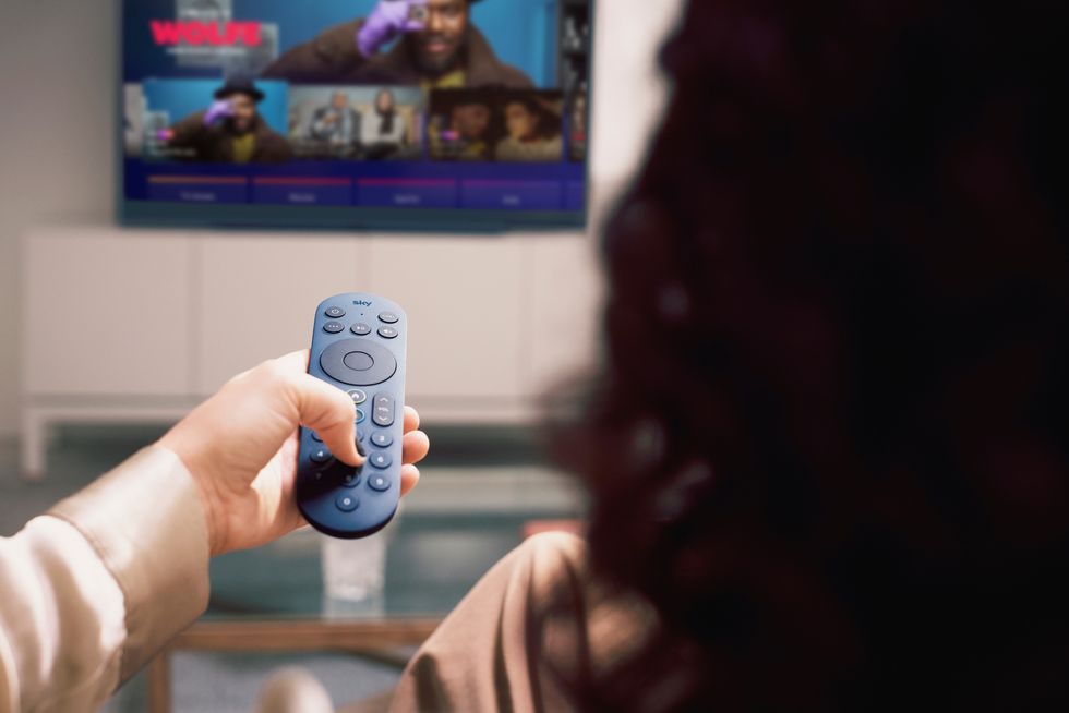 a woman holds up the redesigned sky stream remote control pointed at a television