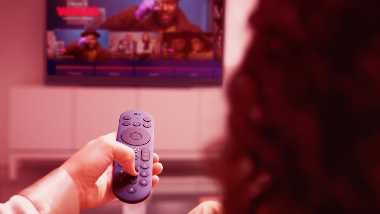 a woman holds up the redesigned sky stream remote control pointed at a television