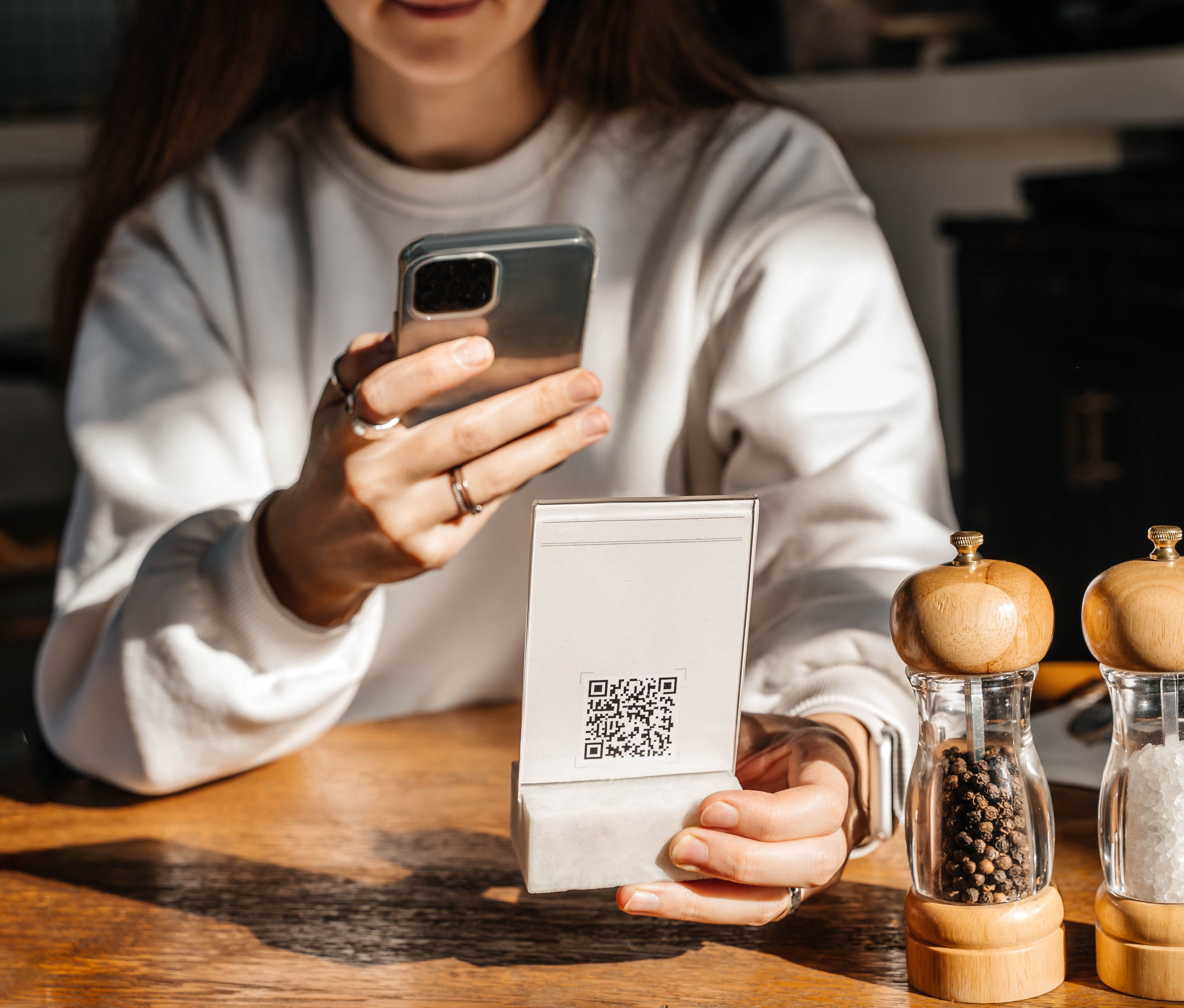 a woman in a grey sweatshirt uses her phone to scan a qr code on a menu