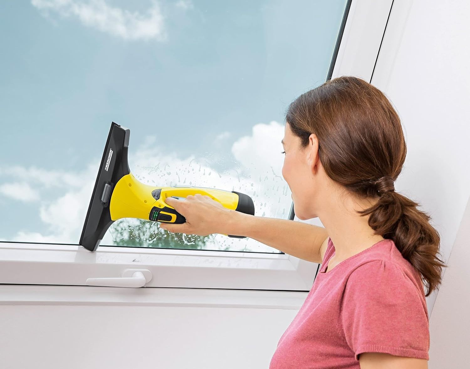 a woman in a pink t-shirt using a karcher window vac to remove water from a window