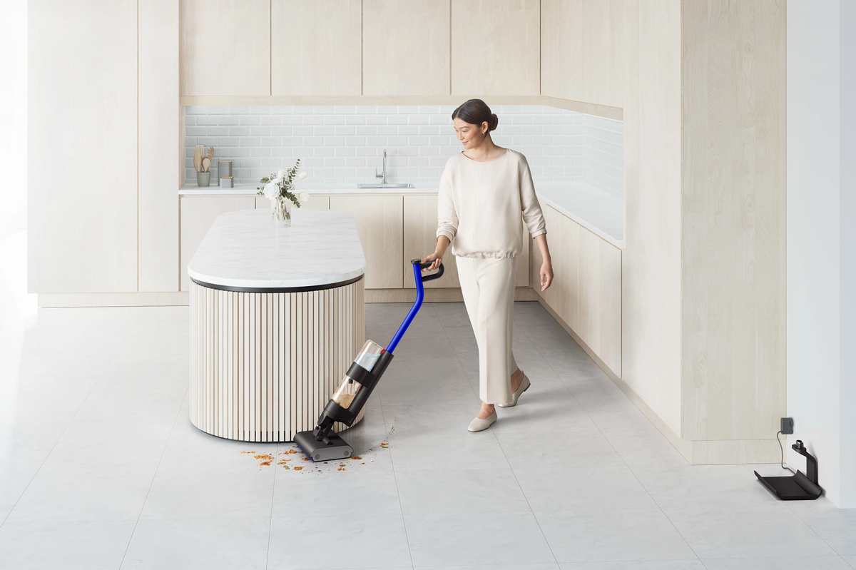 a woman in pictured cleaning around a kitchen island with the wash g1 wet floor cleaner with a charging stand on the right-hand side of the room