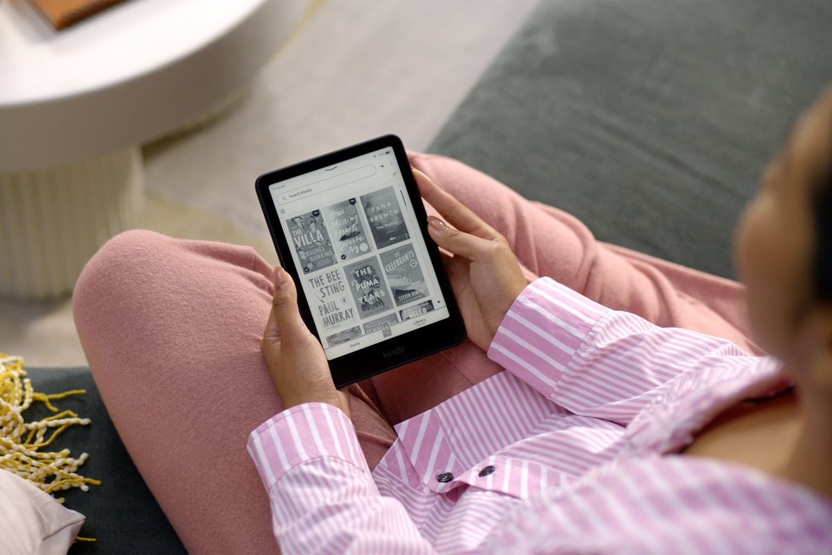 a woman in pink pyjamas sits and reads on a kindle