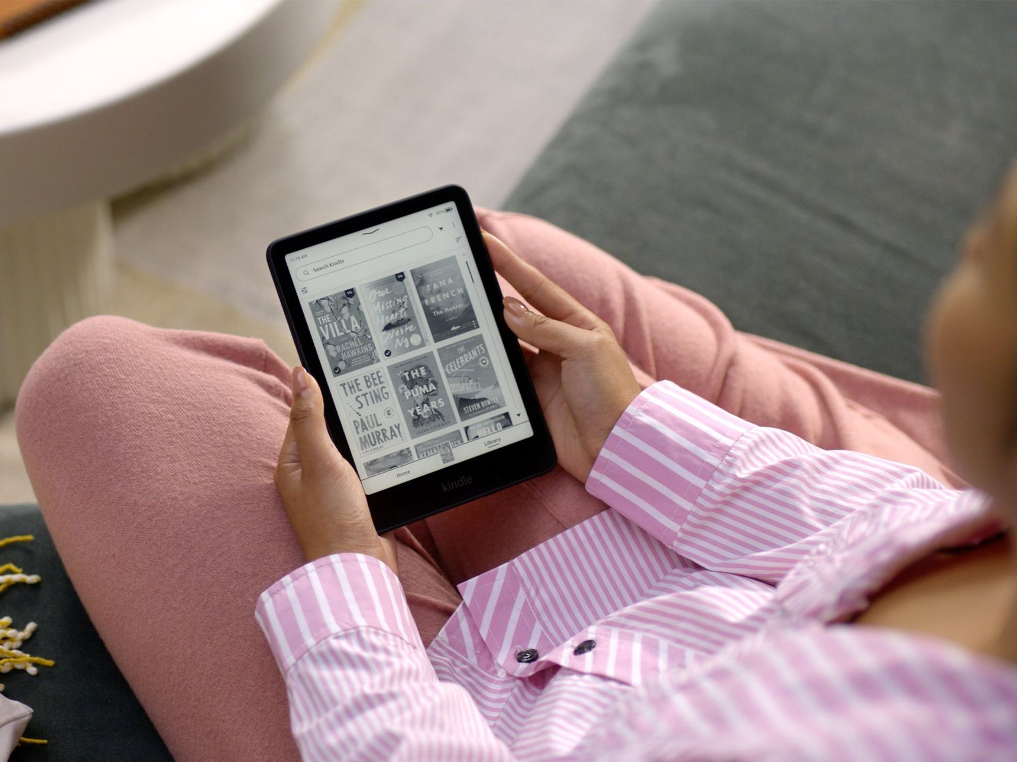 a woman in pink pyjamas sits and reads on a kindle