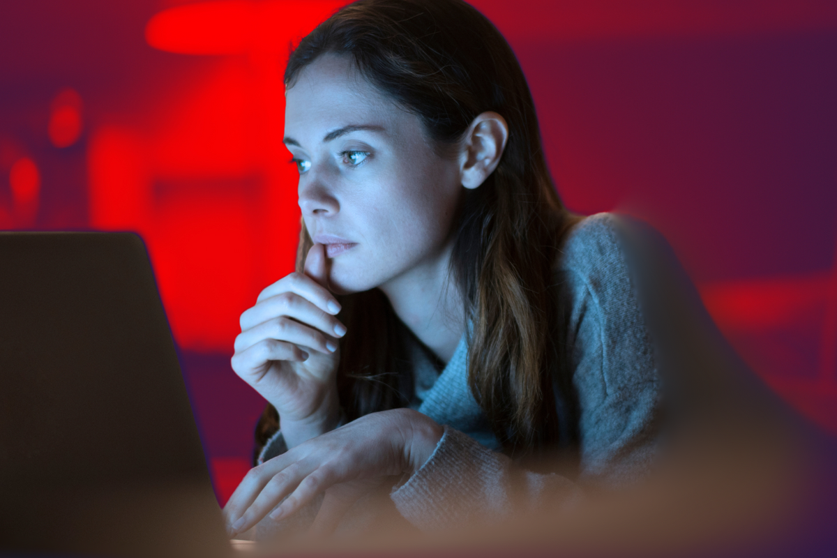 a woman looks concerned sitting in front of her laptop with a red background 