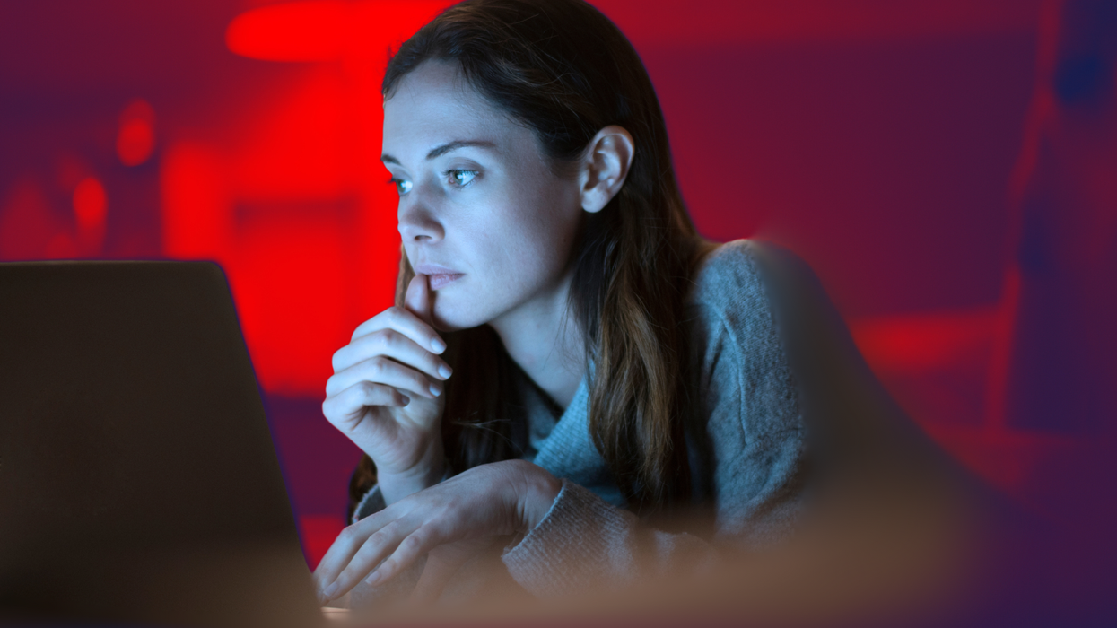 a woman looks concerned sitting in front of her laptop with a red background