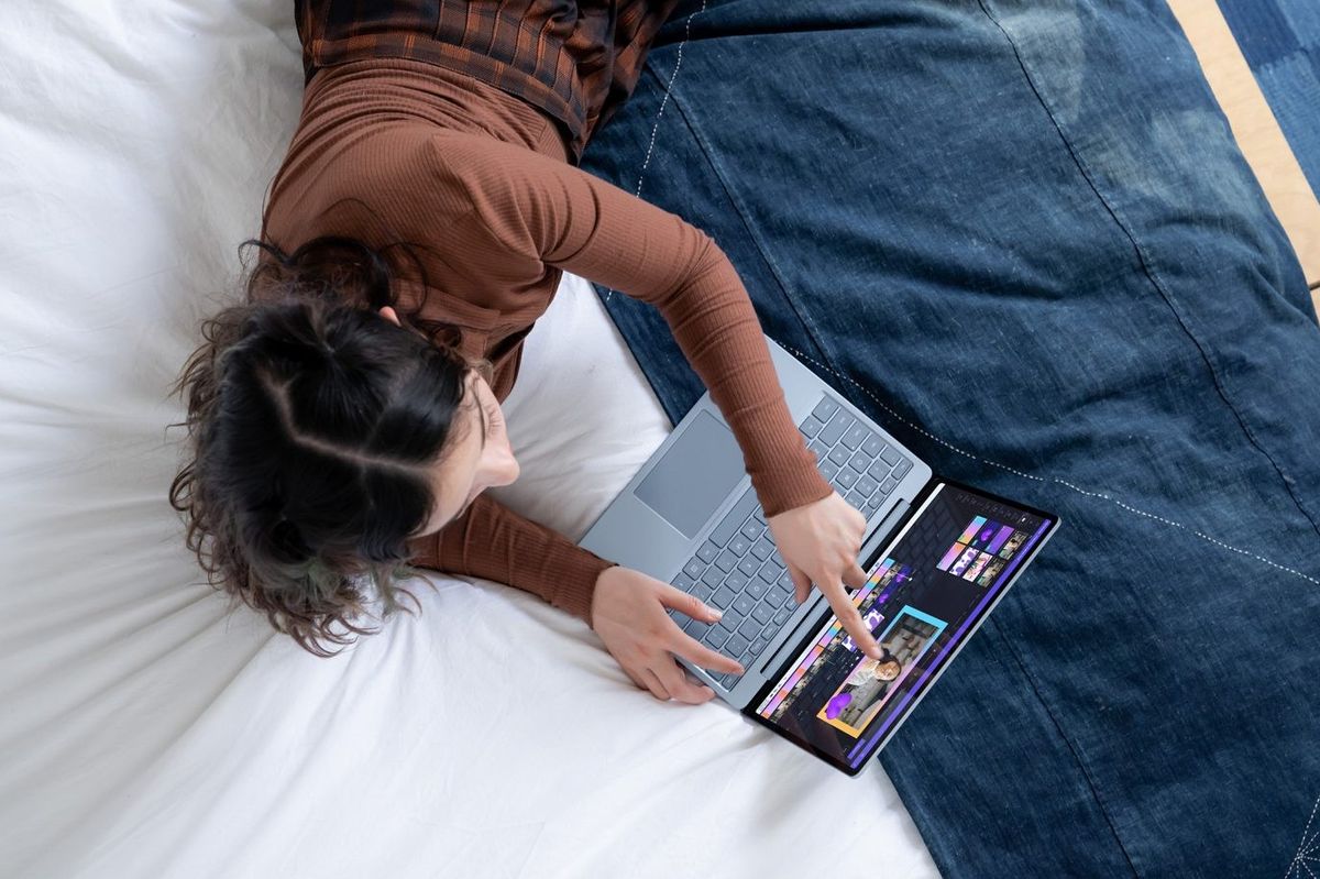a woman lying down on a bedspread using the touchscreen on her surface laptop running windows 11 