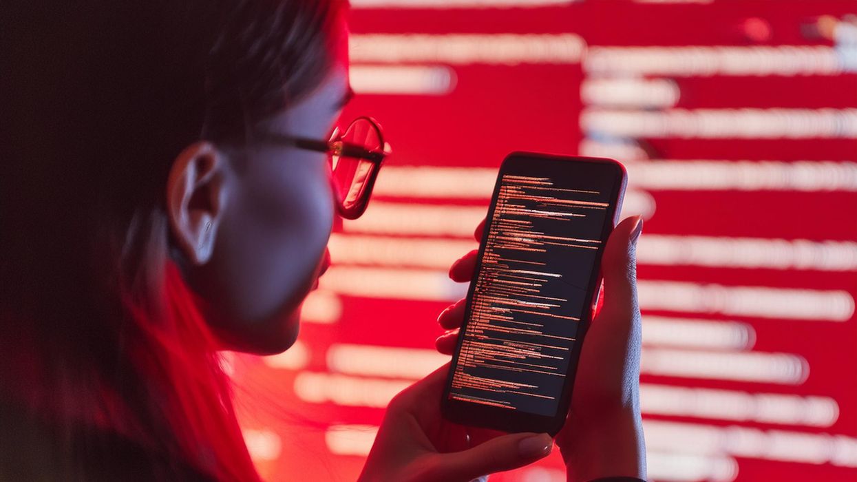 a woman pictured holding her smartphone with lines of red computer code surrounding her