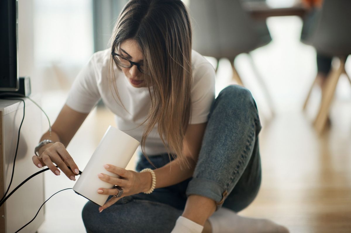 a woman plugs an ethernet cable into the back of a wi-fi router