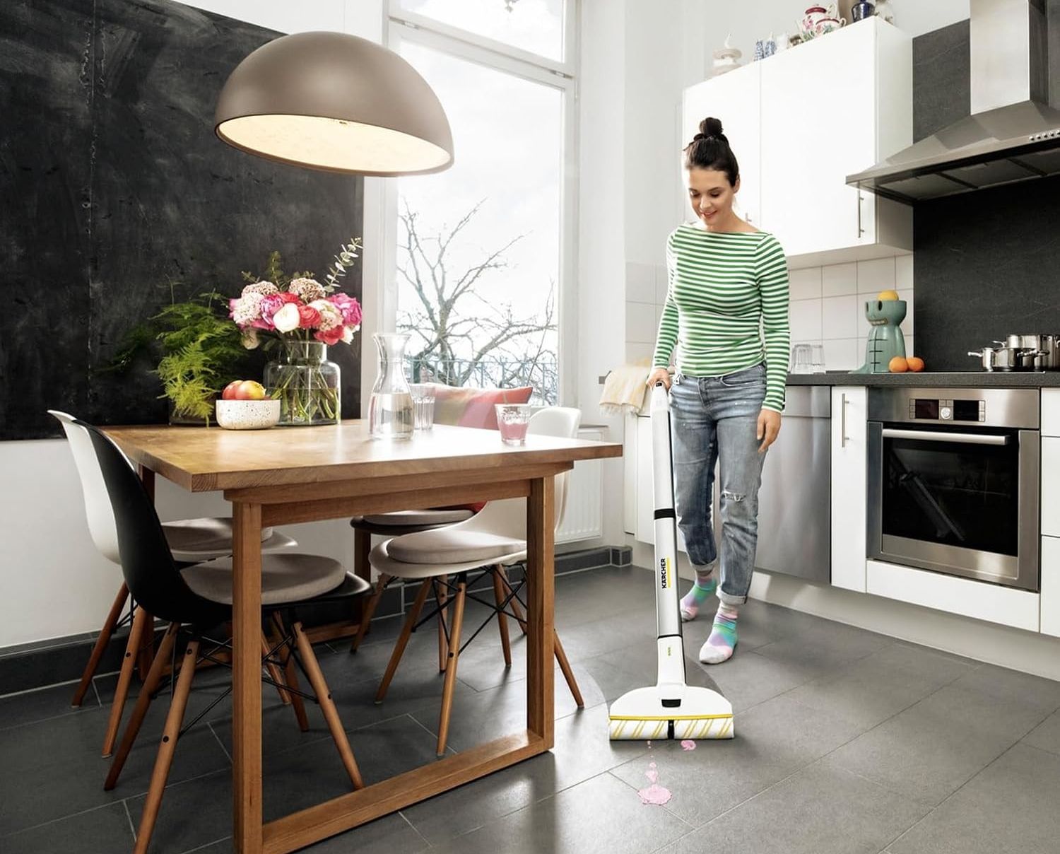 a woman pushes a \u200bK\u00e4rcher EWM 2 Electric Mop in a kitchen with a pink spillage pictured on the floor in the foreground