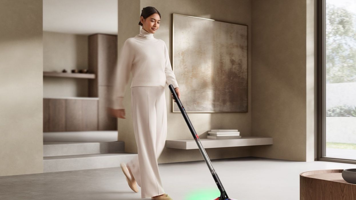a woman pushes the dyson pencilvac on the floor with the laser guides showing at the front and back