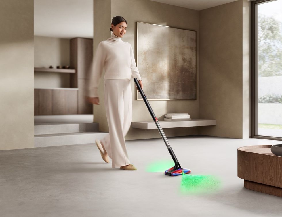 a woman pushes the dyson pencilvac on the floor with the laser guides showing at the front and back