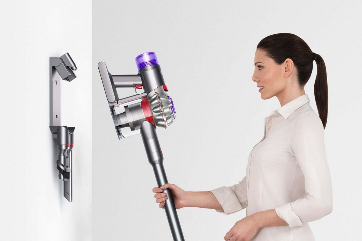 a woman puts the dyson v8 cordless vacuum into the charging dock mounted on a wall