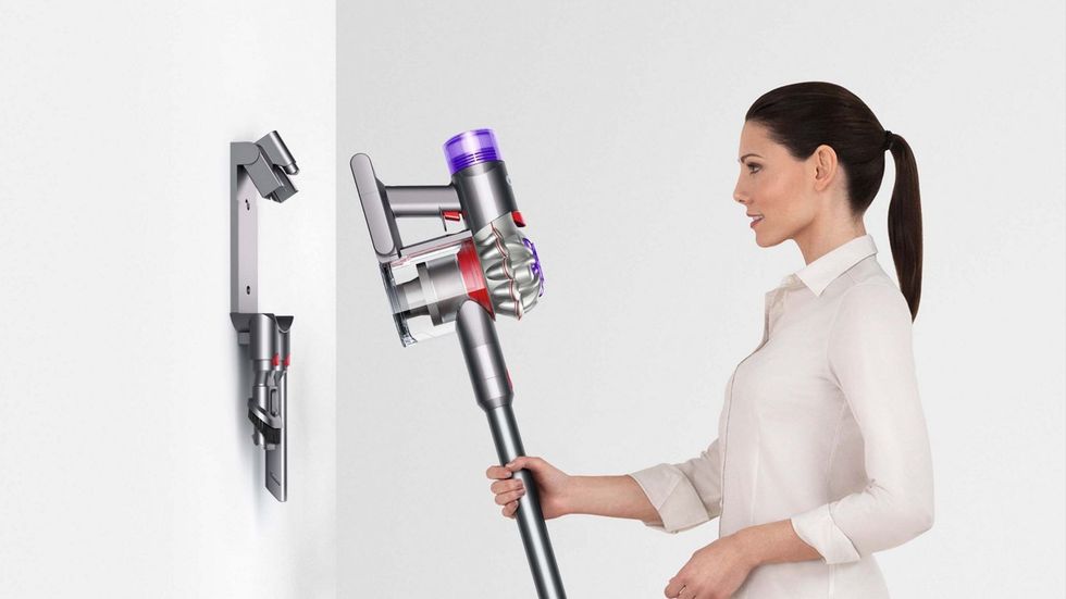 Mulher coloca aspirador sem fio Dyson V8 em base de carregamento montada na parede 