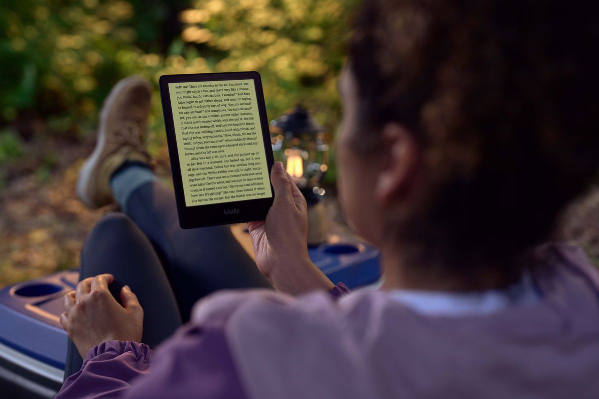 a woman reads on her Kindle with the backlight on outdoors on a camping trip  