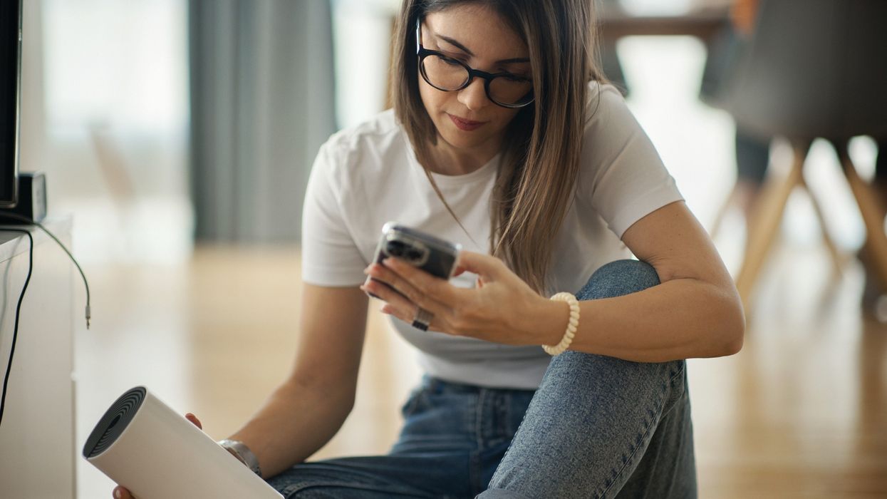 a woman runs a broadband speed test on her phone while holding her wi-fi router sat on the floor
