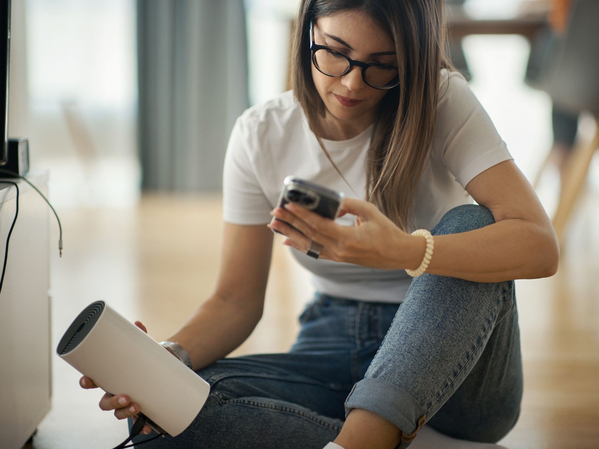 a woman runs a broadband speed test on her phone while holding her wi-fi router sat on the floor